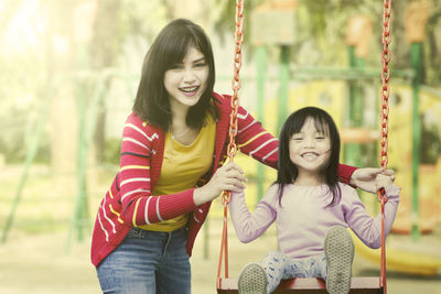 Mother swinging girl at park