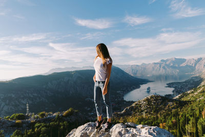 Rear view of woman standing on rock against sky