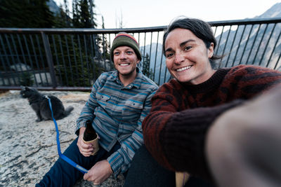 Portrait of smiling friends sitting on railing with their cat on leash