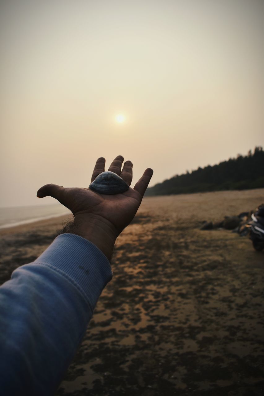 MIDSECTION OF MAN HOLDING SUN OVER BEACH