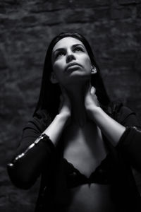 Sad young woman holding her neck while looking up against wall