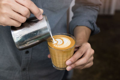 Midsection of man pouring milk in coffee cup