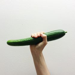 Close-up of hand holding cucumber over white background