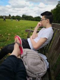 Low section of woman sitting with male friend on bench at park