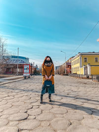 Portrait of woman standing on street against blue sky during sunny day