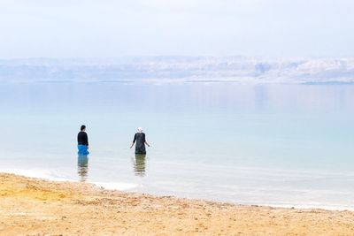 Rear view of women wading in sea against sky