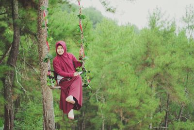 Full length of young woman on swing against trees at forest