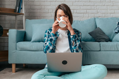 Woman using mobile phone while sitting on sofa at home