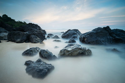 Rocks in sea against sky during sunset