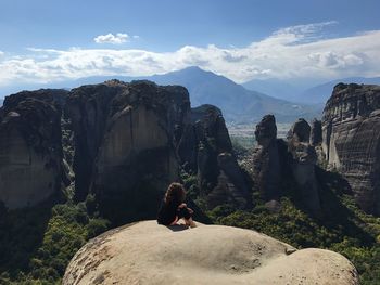 Rear view of woman sitting on rock against sky