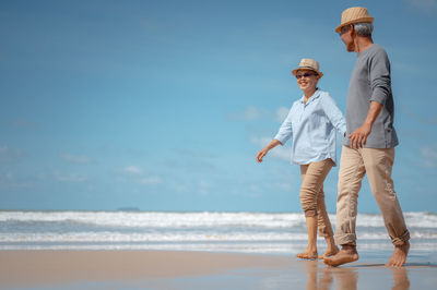 Couple walking at beach against sky