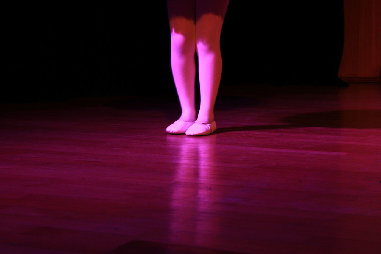 LOW SECTION OF WOMAN STANDING ON ILLUMINATED FLOOR AGAINST BLACK BACKGROUND