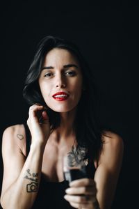 Portrait of smiling woman holding red wine against black background