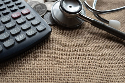 High angle view of calculator and stethoscope by coins on burlap