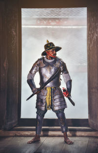 Man in costume holding sword while standing against window