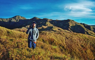 Man standing amidst plants on field against mountains and sky