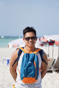 Portrait of man wearing bag while standing at beach against sky