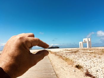 Man holding umbrella on beach against clear blue sky