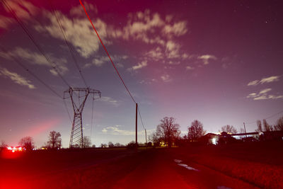 Road by electricity pylon against sky during sunset