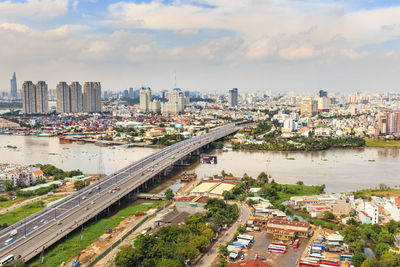 High angle view of bridge and buildings in city against cloudy sky on sunny day