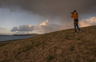 Full length of man photographing on land against sky