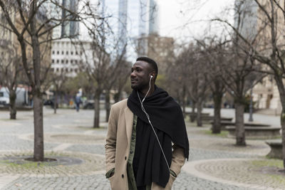 Young man looking away while standing on street in city