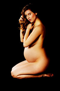 Portrait of naked pregnant woman kneeling over black background