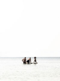 People on floating platform in sea against clear sky