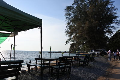 Empty chairs and tables at restaurant by sea against sky