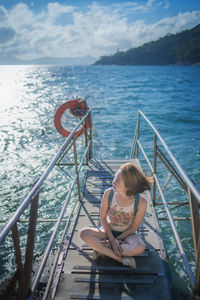 Woman sitting on pier over sea against sky