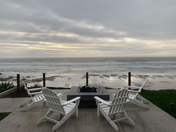 Empty chairs and table on beach against sky