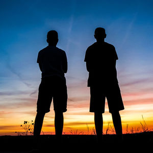 Silhouette men standing on field against sky during sunset
