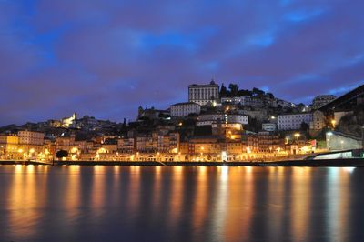 Illuminated cityscape by river against sky at night