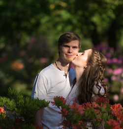 Woman kissing boyfriend standing amidst flowers at park