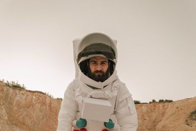 Portrait of man wearing space suit standing against sky