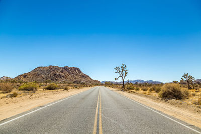 Road amidst trees against clear blue sky