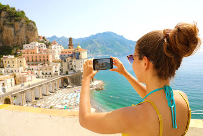 Woman photographing buildings from mobile phone by sea