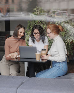 Smiling woman using laptop sitting by friends at cafe