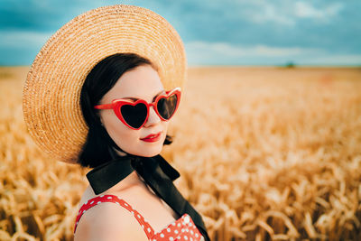 Portrait of young woman wearing heart shape sunglasses against field