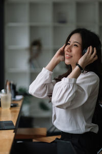 Portrait of young woman using mobile phone while sitting in office