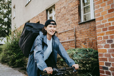 Smiling female biker doing delivery on bicycle at street in city