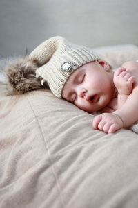 Cute baby girl wearing knit hat while sleeping on bed at home
