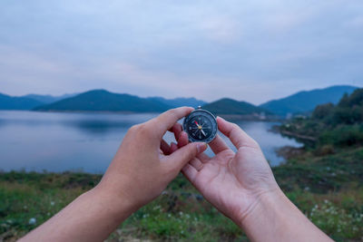 Cropped hands holding navigational compass against lake