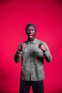 Portrait of young man standing against red background