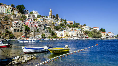Boats moored in sea by townscape against clear blue sky