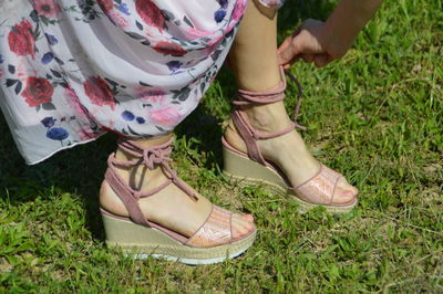 Low section of woman tying sandal lace on grassy field