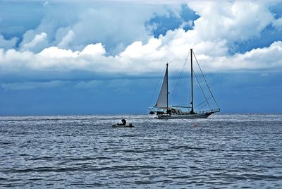 Boats sailing in sea against cloudy sky