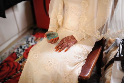 Midsection of bride in wedding dress sitting on chair