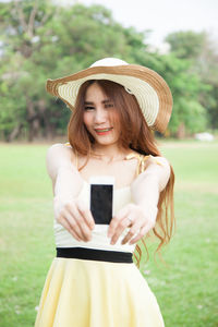 Close-up portrait of young woman holding smart phone while standing on grass field