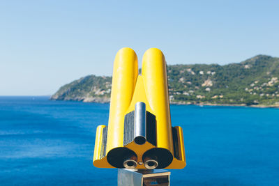 Close-up of yellow coin-operated binoculars against sea